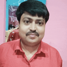 a man with a mustache wearing a red shirt is standing in front of a pink wall