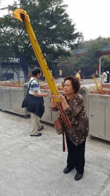 an elderly woman is holding a very long yellow stick