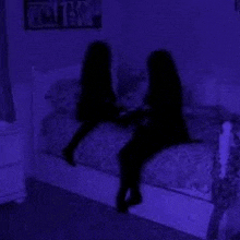 a couple of girls are sitting on a bed in a dark room .