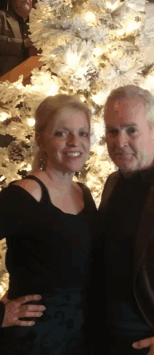 a man and a woman are posing for a picture in front of a christmas tree