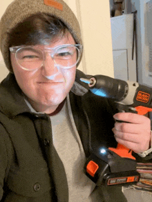 a man wearing glasses and a beanie is holding a black and decker cordless drill