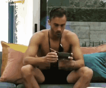 a shirtless man is sitting on a couch looking at a cell phone