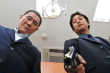 a man in a suit holds a gun in front of another man in a suit