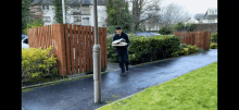 a man is carrying a stack of newspapers on a sidewalk in front of a wooden fence