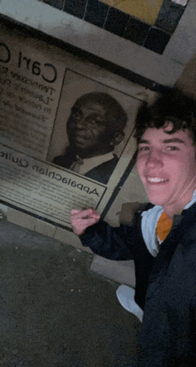 a young man stands in front of a plaque with a picture of a man and the year 1676 on it