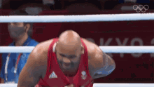 a man in a red tank top is standing in a boxing ring with his hands on his hips .