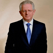 a man in a suit and tie is standing in front of a white wall .