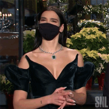 a woman wearing a black mask and a necklace with the letters snl on the bottom right