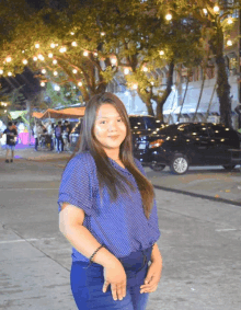 a woman in a blue shirt stands in front of a car parked in a parking lot