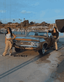 two women standing next to a car that says ' mrznez ' on the side