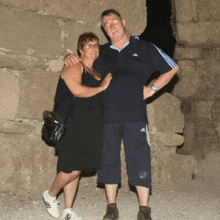 a man and a woman are posing for a picture while standing next to each other in front of a stone wall .