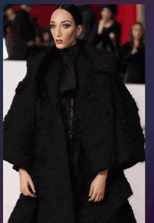 a woman is wearing a black coat with ruffles on the sleeves