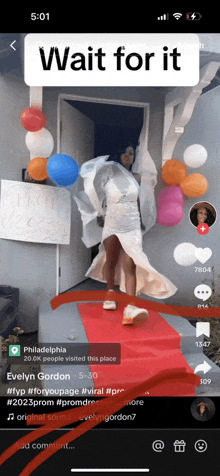 a woman in a white dress is standing on a red carpet with balloons behind her and a sign that says wait for it