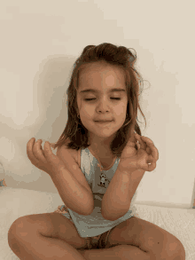 a little girl sits in a lotus position with her eyes closed and her hands folded