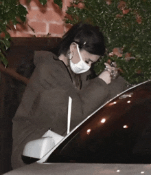 a woman wearing a mask sits in a car looking at her phone