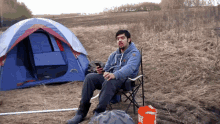 a man sits in a chair in front of a tent and a bucket that says home depot on it