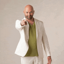 a bald man wearing a white jacket and a green shirt pointing at the camera