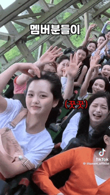 a group of people are riding a roller coaster and one girl is making a heart with her hands .