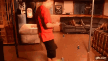 a man in a red shirt is standing in a living room with a couch .