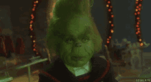 a close up of a grinch 's face in a dark room with christmas lights in the background .