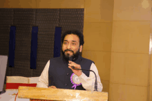 a man stands at a podium speaking into a microphone with a purple ribbon around his neck