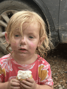 a little girl with a messy face is holding a cupcake with whipped cream on it