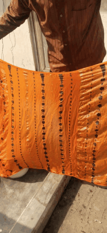 a man in a brown shirt is holding a large orange piece of fabric