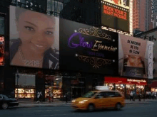 a yellow taxi is driving down a city street in front of a large billboard .