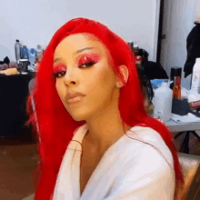 a woman with red hair and red eye shadow is sitting in a chair in a room .