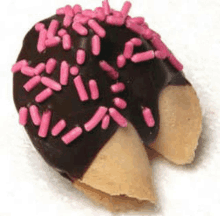 a chocolate covered fortune cookie with pink sprinkles on a white surface