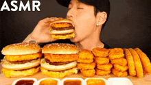 a man is eating a hamburger surrounded by nuggets and sauces