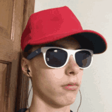 a young man wearing a red hat and sunglasses looks at the camera