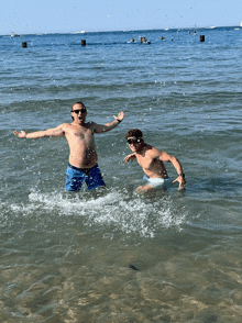 two men are splashing in the ocean and one is wearing sunglasses