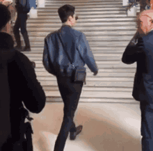 a man in a denim jacket and black pants is walking down stairs .