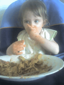 a little girl wearing a bib that says ' baby ' on it eating a plate of food