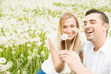 a man and woman blowing dandelions in a field of white flowers