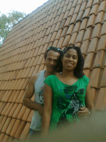 a man and a woman are posing for a photo in front of a tiled roof