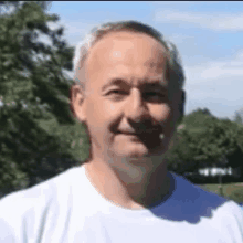 a man with gray hair is wearing a white shirt and smiling .