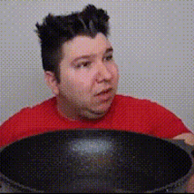 a man in a red shirt is sitting in front of a black pan