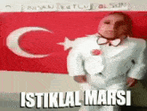 a man in a suit and bow tie is standing in front of a turkey flag and says istiklal marsi