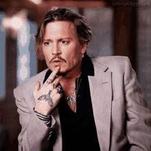 johnny depp is wearing a suit and a black shirt and has a tattoo on his hand .