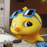 a yellow rubber duck wearing blue square sunglasses sits on a bathroom counter