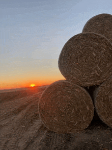 bales of hay are stacked on top of each other in a field at sunset