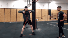 a man in a black shirt with the word army on it stands next to another man in a gym