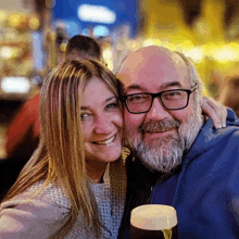 a man with glasses and a beard holds a glass of beer next to a woman