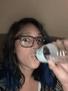 a woman wearing glasses is drinking water from a bottle