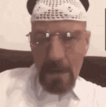 a man with a beard and glasses is wearing a white hat and a white shirt .