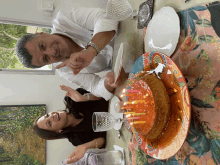 a man and a woman are sitting at a table with a cake and candles