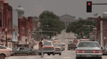 a man in a cowboy hat stands in the middle of a busy street with a red light in the background