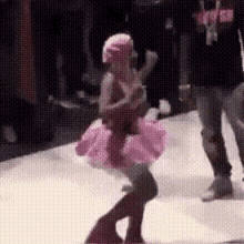 a little girl is dancing on a stage wearing a pink tutu .